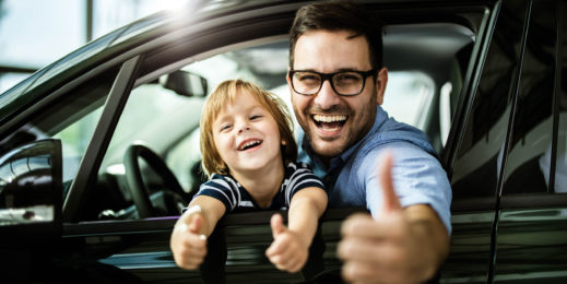 Happy single father and son testing new car in a showroom and showing thumbs up.